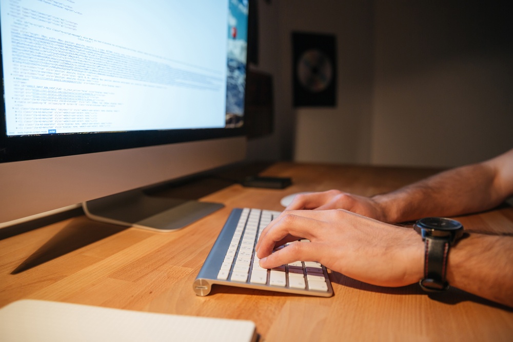 Closeup of keyboard and monitor of computer used by young man on wooden table